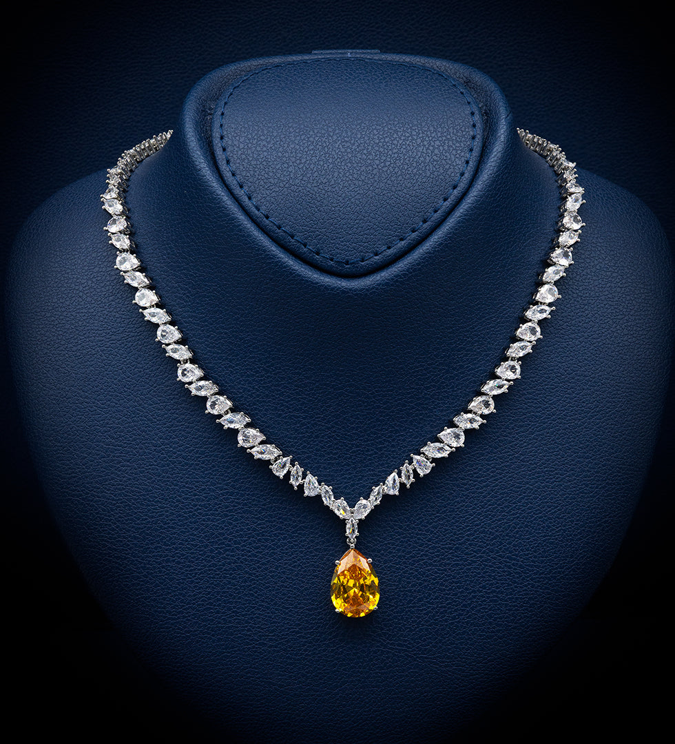 A diamond necklace displayed on a dark blue jewelry bust, featuring a pear-shaped yellow gemstone pendant.